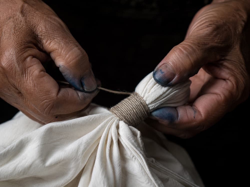 Hands binding cotton fabric with string, preparing it for shibori dyeing