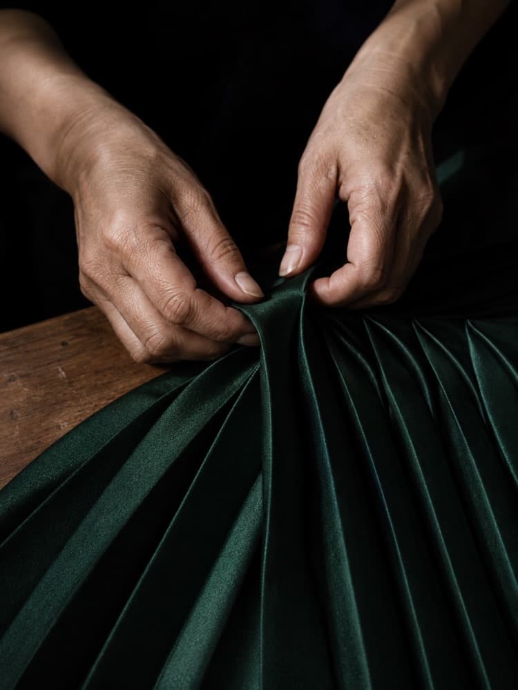 Hands pressing a knife-pleat into deep emerald fabric